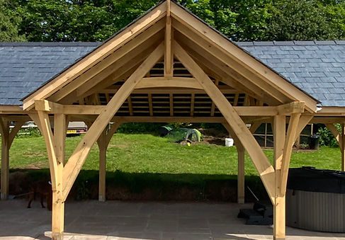 Oak wooden gazebo structure with a gabled roof in a garden setting.