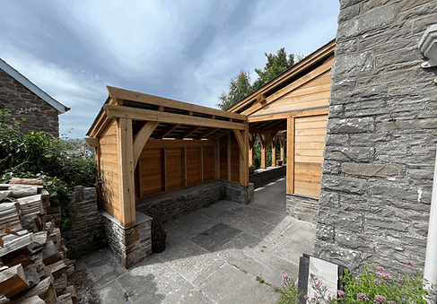 A wooden oak carport attached to a stone building under a cloudy sky.