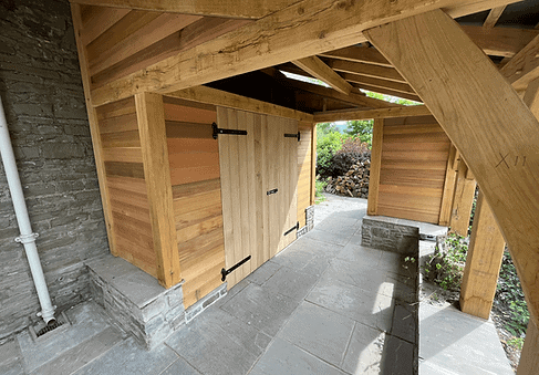 A wooden, barn-style door under an oak-framed shelter with stone flooring.