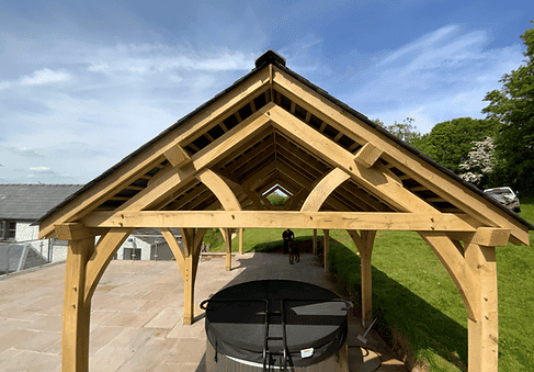 Oak wooden gazebo structure with exposed beams and a triangular design on a sunny day.