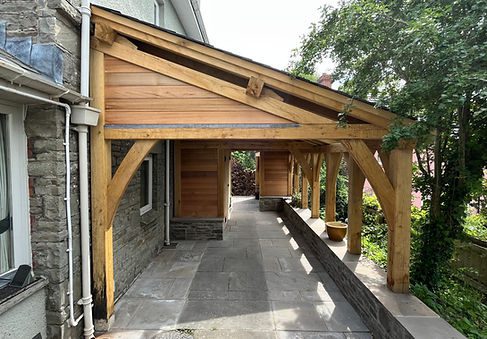 A wooden lean-to structure made of oak with a sloped roof attached to a stone building, providing a covered outdoor walkway.