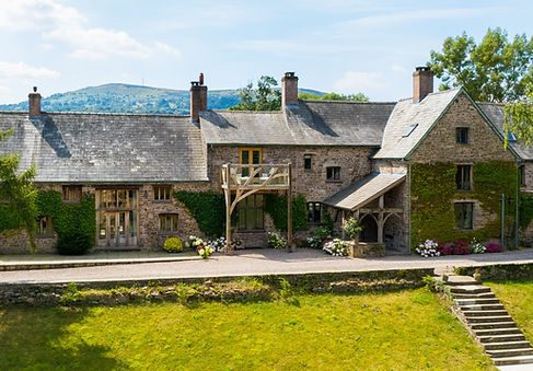Traditional stone cottages with slate roofs and oak beams in a rural setting on a sunny day.