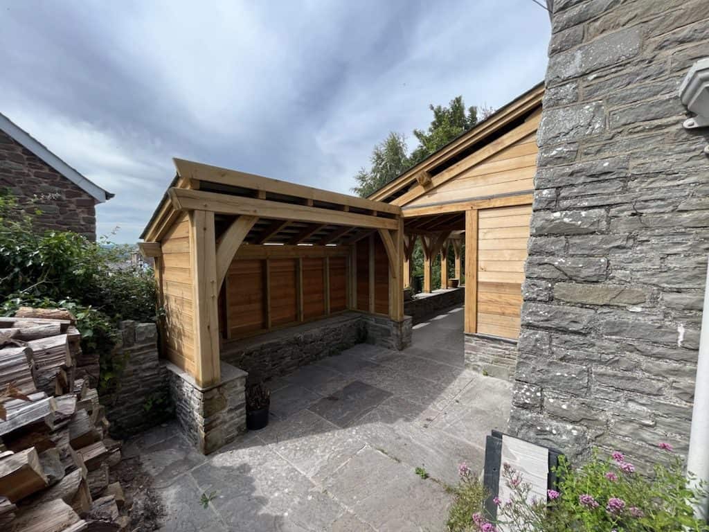 New oak wooden carport attached to a stone house under a cloudy sky.