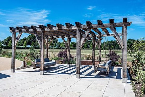 An oak wooden pergola with integrated benches in a park on a clear day.