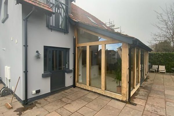 Newly constructed oak wooden conservatory attached to a blue house with a tiled patio area.