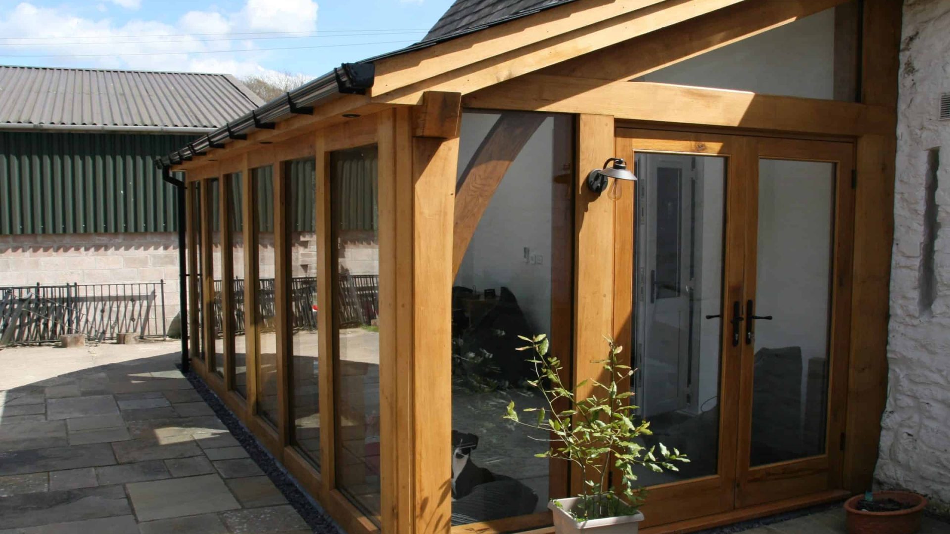 Sunlit oak conservatory attached to a stone house with open French doors.