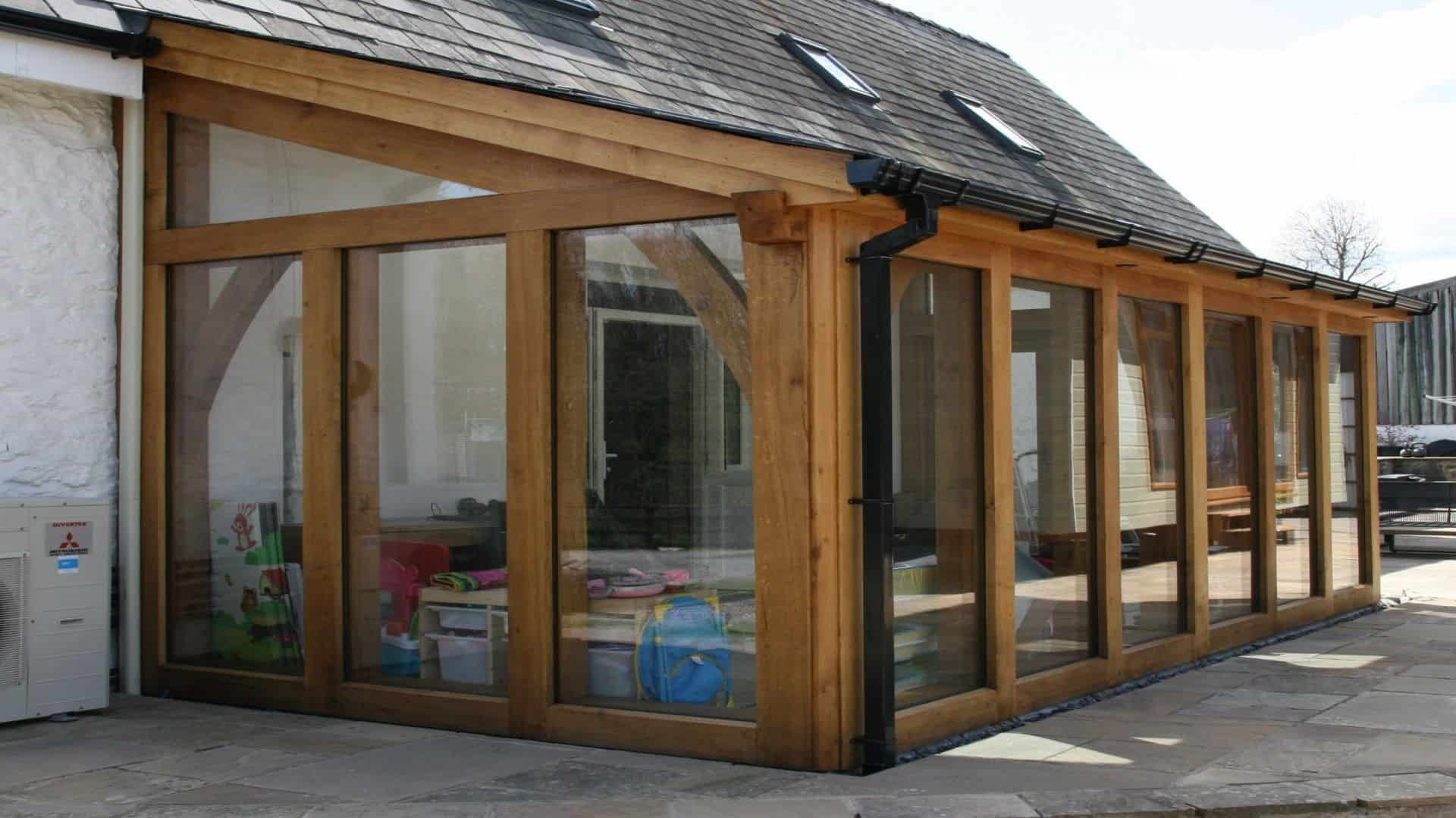 A modern conservatory with large glass windows and an oak wooden framework attached to a stone house.