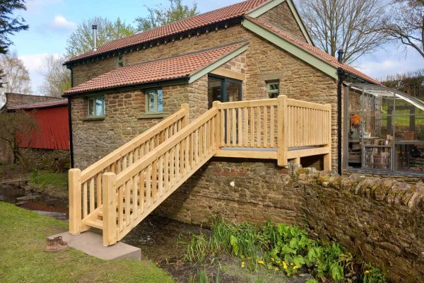Stone cottage with a new oak staircase leading to the upper entrance and a glass conservatory on the side.
